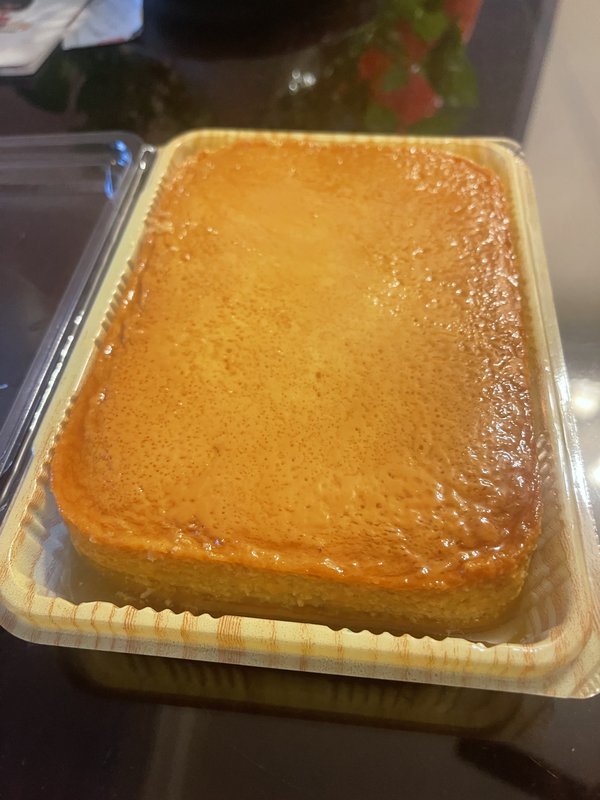 Caramel Custard: a rectangular golden-brown baked custard with a glossy caramel top, served in a disposable aluminum foil tray.