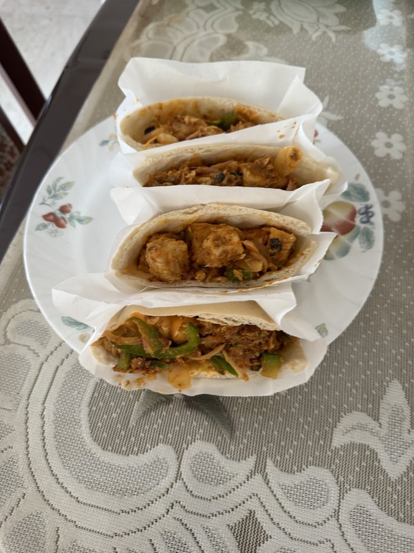 Chicken Pita Pockets: four pita breads filled with spiced chicken, green peppers, and onions in a reddish-orange sauce, wrapped in parchment paper, served on a floral white plate.