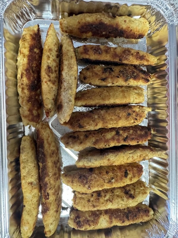 Chicken Seekh Kabab: elongated ground chicken kebabs, lightly charred and golden-brown, arranged in rows on a foil tray, no garnishes or accompaniments visible.