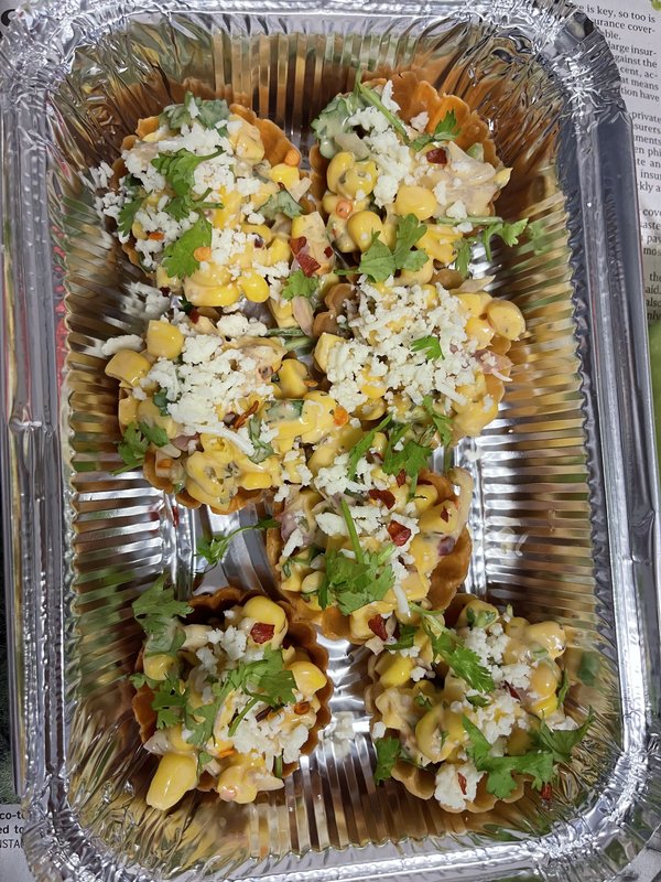 Cheese Corn Canopies: crispy tart shells filled with corn and cheese, topped with crumbled white cheese, chopped cilantro, and red spice flakes, arranged in a foil tray.
