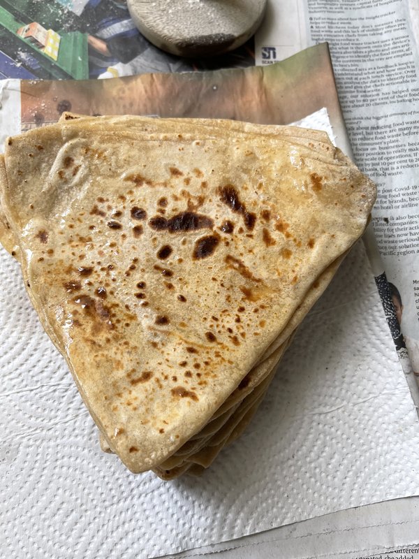 Plain Paratha: a stack of folded, golden-brown whole wheat flatbreads with charred spots, resting on paper towels over newspaper.