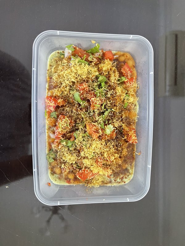 Ragda Pattice: two pan-fried potato patties in a container, served with a bowl of white pea curry, chopped onions, tomatoes, cilantro, and green chutney.