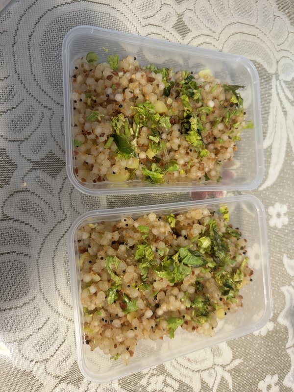 Sabudana Khichdi: two plastic containers filled with cooked tapioca pearls mixed with mustard seeds, peanuts, green chilies, and garnished with fresh cilantro.