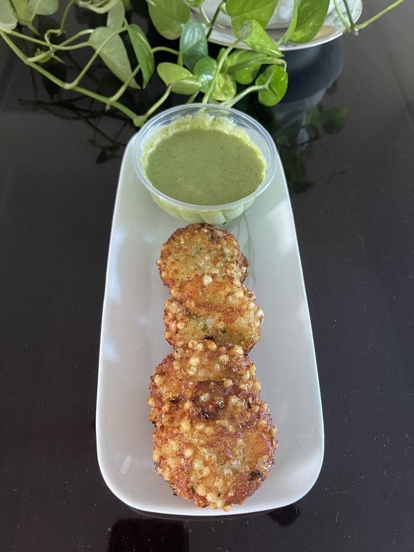 Sabudana Vada: six golden-fried tapioca and potato patties flecked with green herbs, arranged in a row on a white rectangular plate.