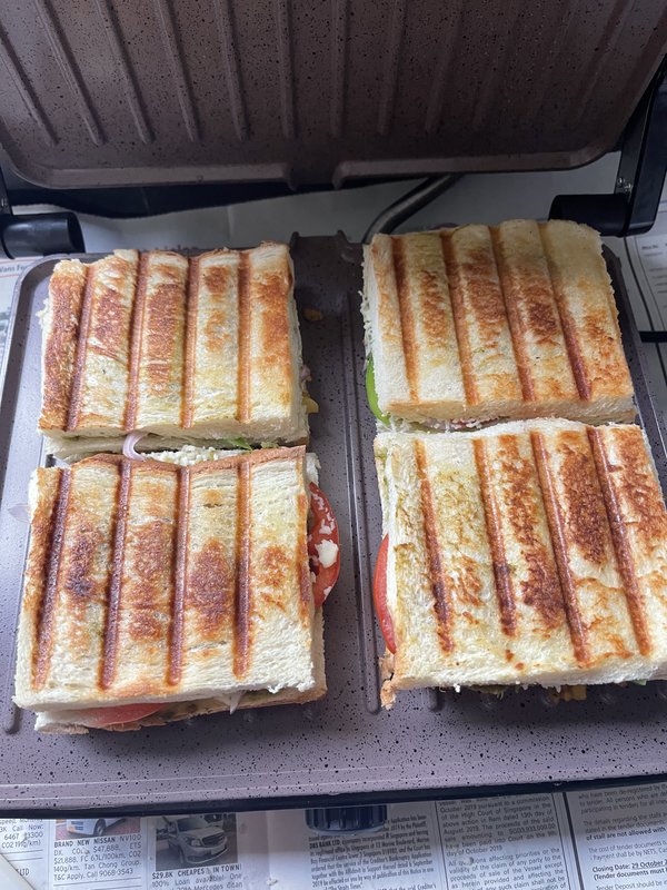 **Grilled Veg Club Sandwich:** Open-faced white bread slices spread with green chutney and spiced mashed potato filling, arranged in two rows on a plastic-covered surface, ready for assembly.