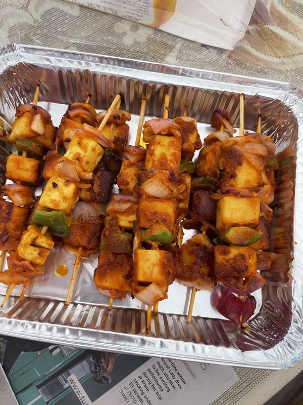 Paneer Tikka skewers with cubed paneer, green bell peppers, and red onion, coated in orange-red spiced marinade, arranged in a foil tray.