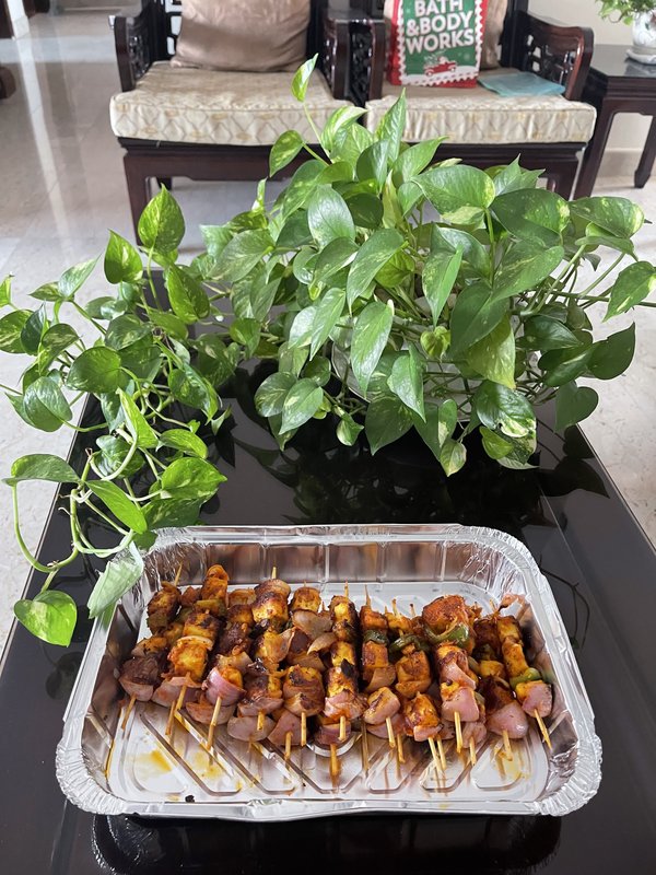 Paneer Tikka skewers with cubed paneer, green bell peppers, and red onion, coated in orange-red spiced marinade, arranged in a foil tray.