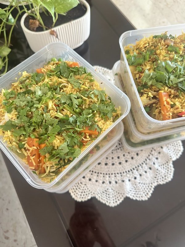 Veg Pulao in a clear plastic container with yellow basmati rice, diced carrots, green peas, and generous fresh cilantro garnish.