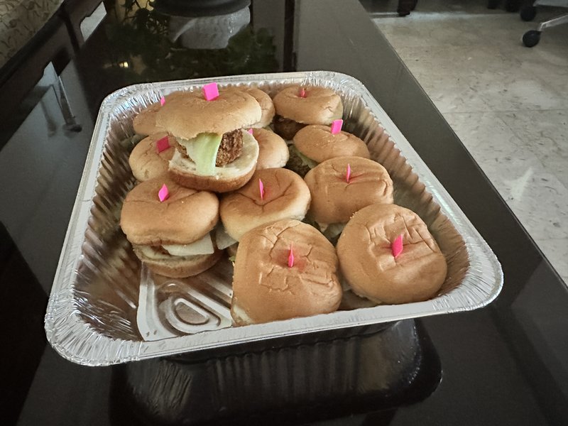 Mini Veg Burger (Sliders): small soft buns filled with veggie patties and lettuce, each marked with a pink toothpick flag, arranged in a foil tray.
